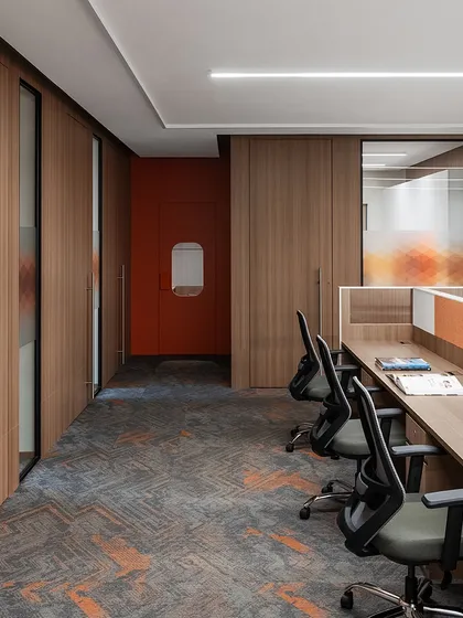 A corridor view in 'The High-Flying Office' shows the flow between the open workstation area and private cabins. The design uses a consistent material palette of wood-look laminate and carpet with rust orange accents to unify the space.