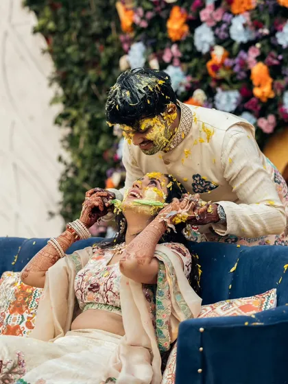 The groom playfully smears haldi on the bride's face during their ceremony. This candid action shot is filled with energy and happiness.