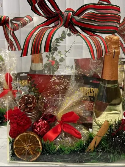 A perfect Christmas hamper, featuring sparkling wine, Hershey's chocolates, a scented candle, and festive decorations like dried orange and cinnamon.