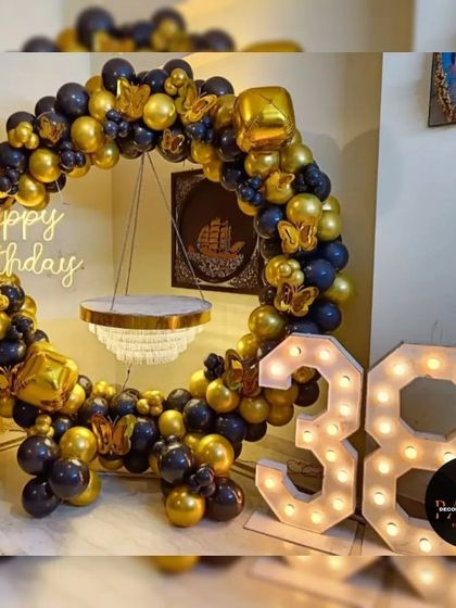 A classy ring decoration for a 38th birthday, using black and gold balloons with butterfly accents and marquee numbers.