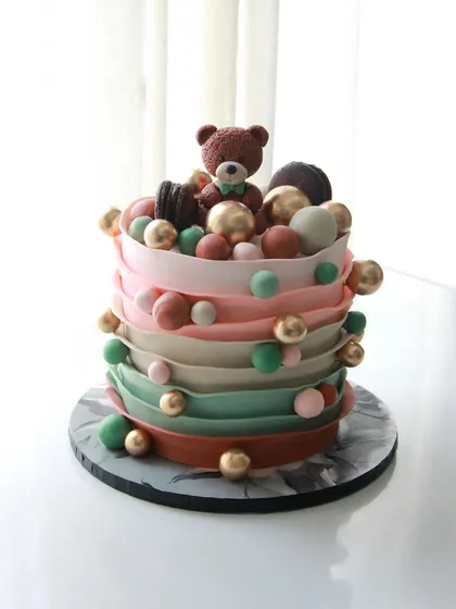 A playful baby shower cake with colorful ruffles and a cute teddy bear on top.