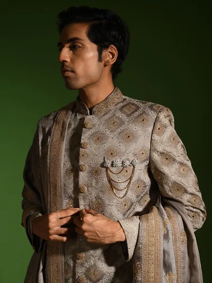 A side profile of the steel grey sherwani, showing how the intricate pattern flows across the garment. The precise tailoring around the shoulders and collar ensures a sharp, defined silhouette.