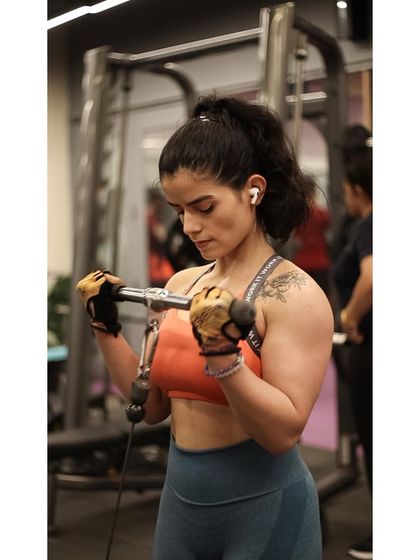 A member shows her defined arm muscles while doing cable curls, a great exercise for constant tension on the biceps.