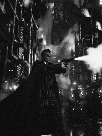 A character in a trench coat fires a gun in a dark, steaming alley in 'Bombaytron'. This image leans heavily into the classic crime and noir film tropes that inspire the series.