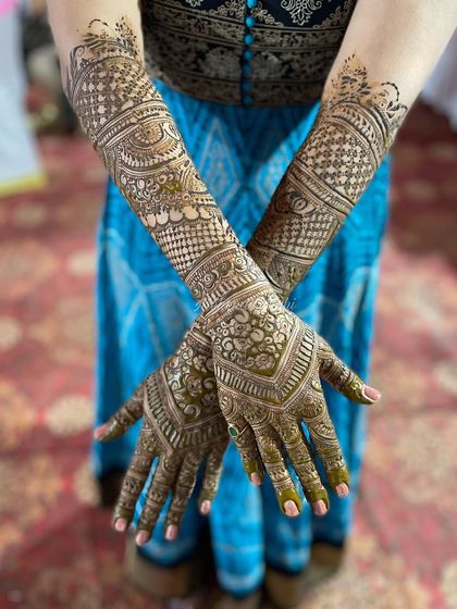 A lovely crossed-arm pose showing the full extent of the bridal henna. The design is consistent across both arms, featuring floral bands and intricate fillers.