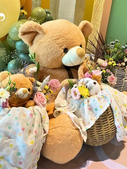 A family of teddy bears ready for the barnyard party. The large bear holds smaller bears in baskets, all adorned with fresh flowers, creating an adorable and heartwarming decor piece.
