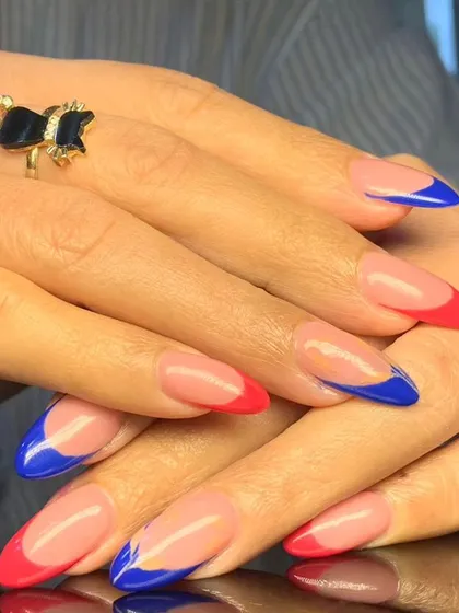 A bold and artistic French manicure combining bright red and royal blue tips in abstract, wavy patterns.