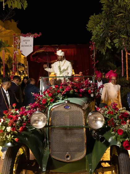 The groom makes a grand entrance in a vintage car, adorned with red roses, blending classic style with royal tradition.