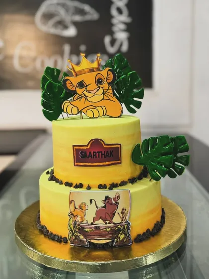 A two-tiered Lion King cake for a young fan. This design features Simba and other characters from the pride lands, decorated with edible leaves for a jungle feel.