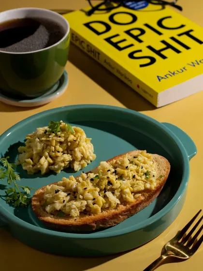 A bright and cheerful breakfast scene with scrambled eggs on toast and black coffee. The colorful plating and props create a happy morning vibe.