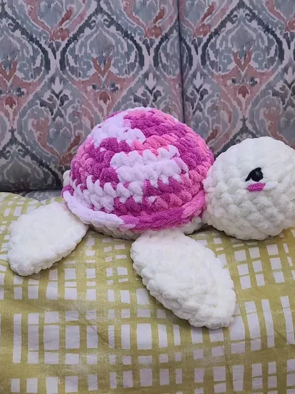 A close-up of a custom turtle with a pink and white variegated shell. You can also see the little eyelashes I added, which is a customization option for any of my plushies to give them a distinct look.