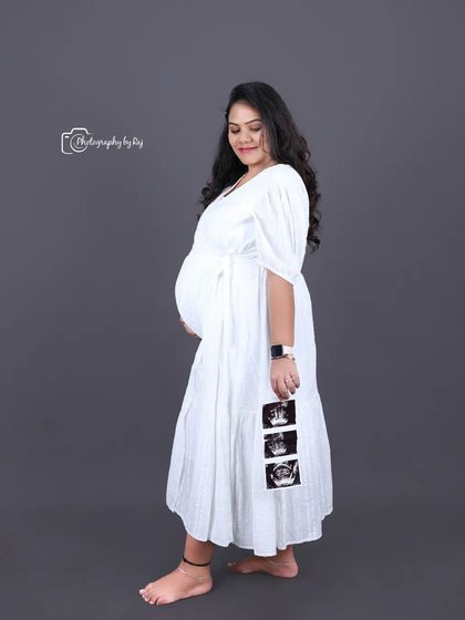 A sweet studio portrait of a mother-to-be holding her ultrasound pictures, wearing a simple white dress.