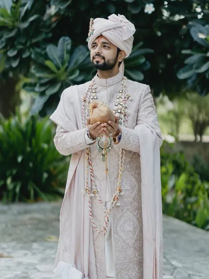 A full-length shot of the groom in his elegant sherwani, holding the sacred coconut.