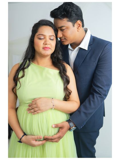 A close-up shot focusing on the deep connection between the expecting parents. Her in a one-shoulder lime green gown, him embracing her from behind, their hands gently resting on the baby bump.