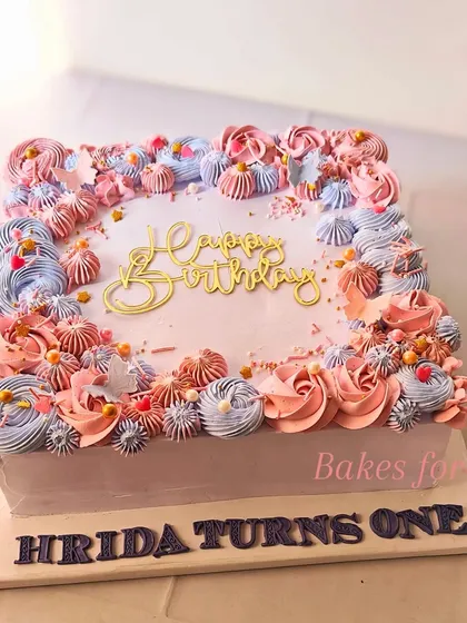 A square smash cake for a first birthday, decorated with a beautiful array of pink and blue piped flowers.