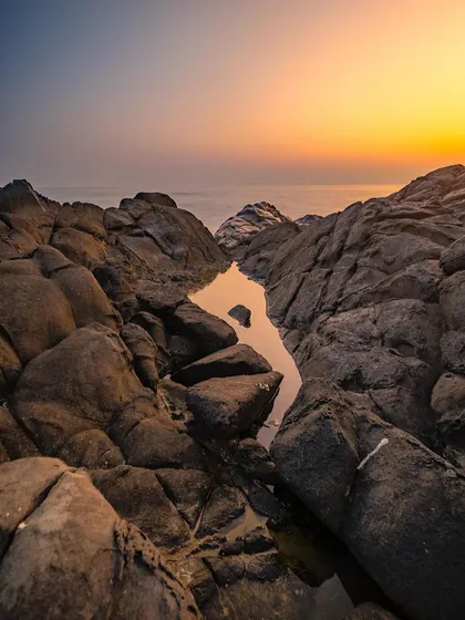 A vertical composition of a rocky shoreline at sunset, focusing on the warm glow and the interesting shapes of the rocks.