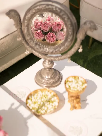 A creative detail shot, with the reflection of pink roses captured in an ornate silver mirror on the table.