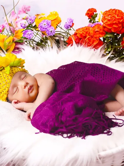 A colorful shot of a sleeping baby surrounded by bright orange, yellow, and purple flowers.