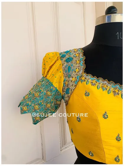 A side view of the yellow puff sleeve blouse. This angle shows the volume of the sleeve and the detailed embroidery on the teal-colored cuff, which adds a unique design element.