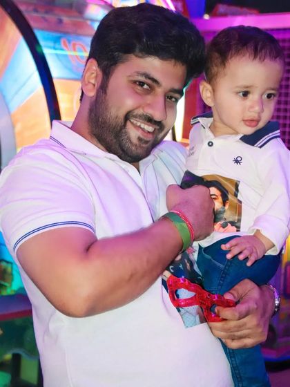 A father holds his young son, who is looking off-camera with a curious expression. This candid shot captures a natural moment at a fun event.