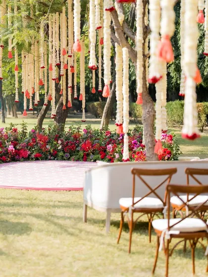 A serene seating area in a garden, with chairs arranged for a ceremony under trees adorned with hanging jasmine and rose tassels.