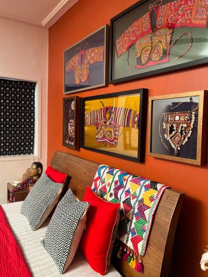 A shot of the headboard, showcasing a collection of framed vintage textiles, including Kapdu and other ethnic embroideries, alongside a colorful patchwork throw.