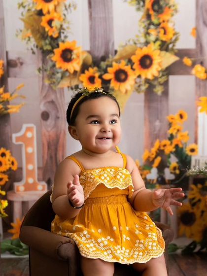 A joyful baby claps her hands during her vibrant sunflower-themed photoshoot.