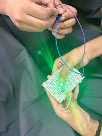 Success! A student holds up a breadboard with a glowing green LED, showing a completed circuit from one of our introductory electronics lessons.