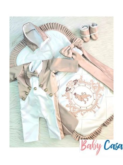 A truly regal set for a little prince. This beige and white tuxedo romper is paired with a matching wrap featuring a lion crest, frilled border, and a beautiful bow.