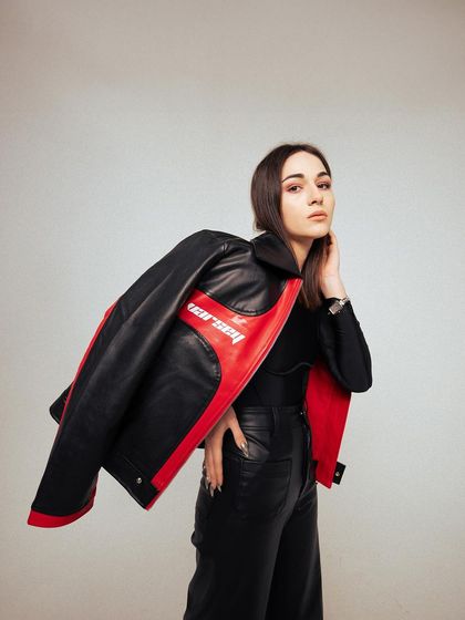 A chic studio shot of a red and black leather jacket. The model's pose, with the jacket draped over her shoulder, gives it a cool, effortless feel.