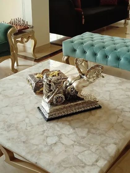 A close-up of a custom coffee table with a beautiful marble top and intricate base. The decorative silver centerpiece adds a touch of opulence to the living room setting.