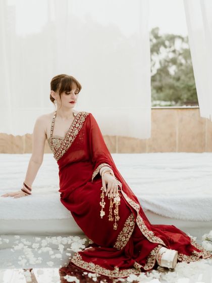 An elegant portrait of the bride in a stunning red saree, seated in a serene, white setting in Jammu. The image is quiet and contemplative, highlighting her grace and beauty.