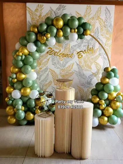 A nature-inspired 'Welcome Baby' setup with an olive green and gold balloon arch against a leafy backdrop.