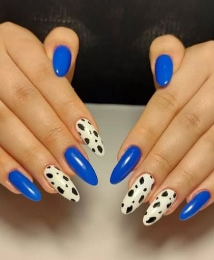 A bold combination of glossy royal blue and a classic black and white cow print on almond-shaped nails.