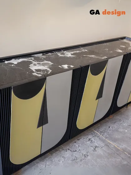 The finished custom-designed console, featuring fluted details and metallic, abstract face-like patterns on the shutters. The black marble top adds a final touch of luxury.