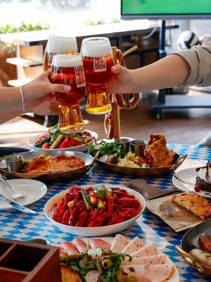 A "cheers" moment with glasses of beer over a table laden with food, capturing a fun, social atmosphere at a sports bar.