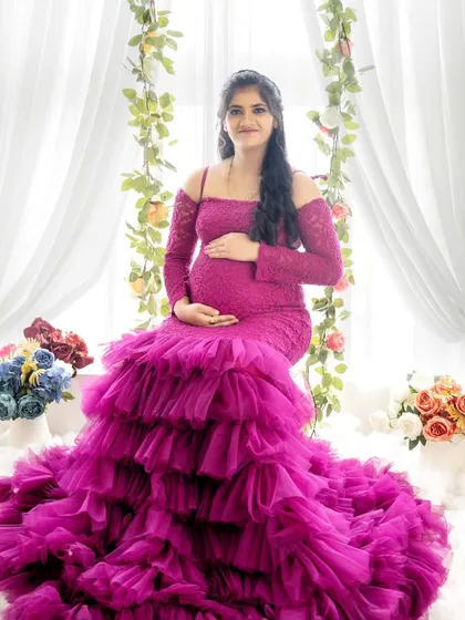 A joyful portrait of a mom-to-be seated on a floral swing, surrounded by a cloud-like floor and draped curtains.