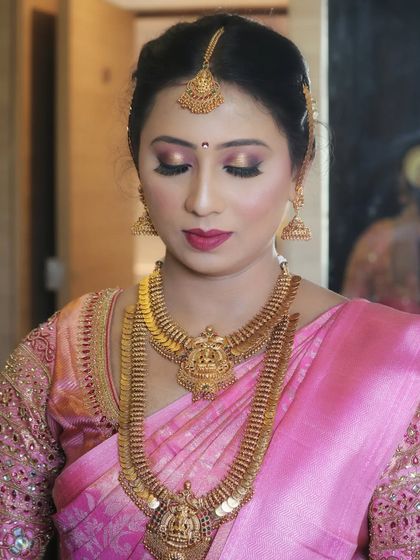 A close-up of a flawless bridal look. The eye makeup is a soft, shimmery pink, paired with a matching lip color and beautiful temple jewellery, perfect for a Kanchipuram silk saree.