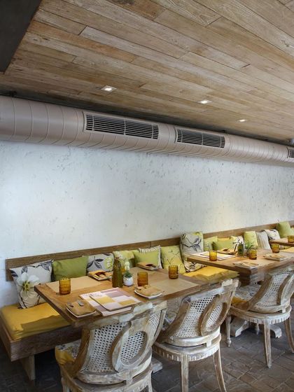 The banquette seating at Amour Bistro is adorned with colorful, patterned cushions, adding comfort and visual interest. The exposed air conditioning duct is painted to blend with the wall, an example of our minimalist and functional design approach.
