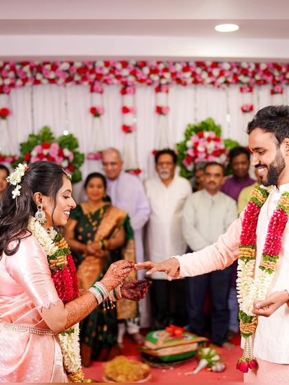 The ring exchange. A close-up of the bride's side profile shows her intricate hairstyle with fresh flowers and her perfectly blended makeup.