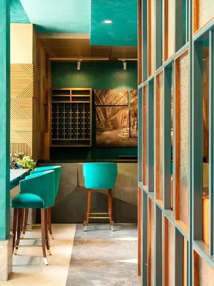 The bar area at The Restaurant at Hibiscus, featuring teal bar stools and a custom wine rack. The design uses partitions of fluted and textured glass to create intimate zones within the larger space.