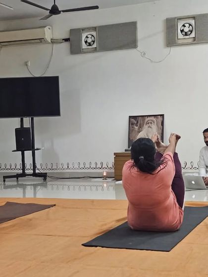 The teacher guides two participants through a challenging core-strengthening posture in Angamardana.