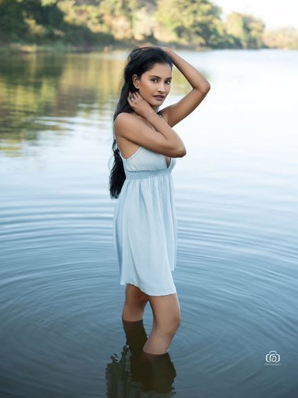 A beautiful portrait of a model in a light blue dress, standing in the calm water of a lake. The reflection of the sky on the water creates a serene and picturesque scene.