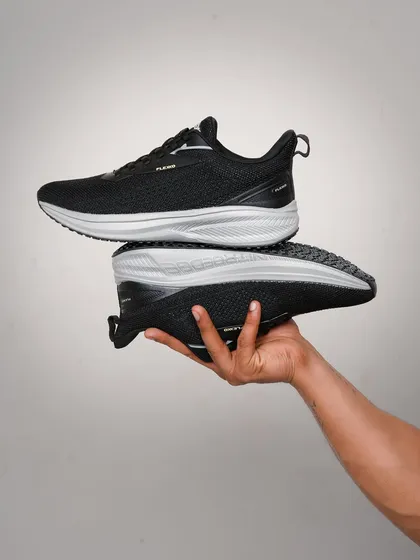 A hand-held shot showcasing a pair of black running shoes. This pose gives a clear view of the shoe's profile and sole, highlighting its design and structure in a simple, clean way.