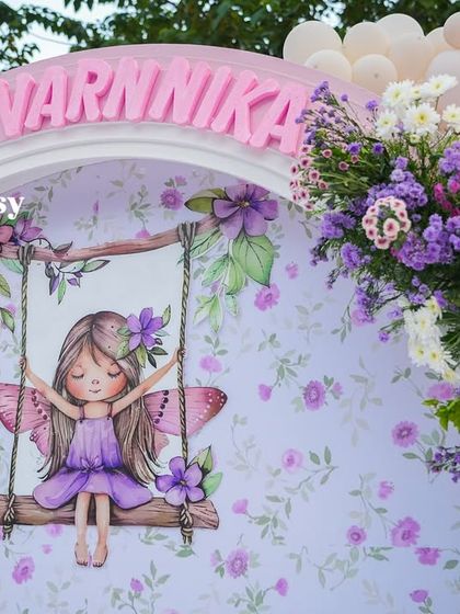 A close-up of the fairy-themed backdrop for Varnnika's party, showing a beautiful illustration of a fairy on a swing.