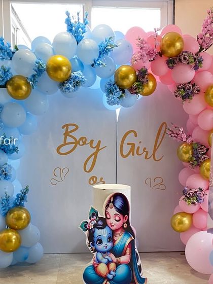 A creative 'Boy or Girl' gender reveal setup with a Krishna and Radha theme. The decor is split into blue and pink sections with matching balloon arches, character cutouts, and floral accents.