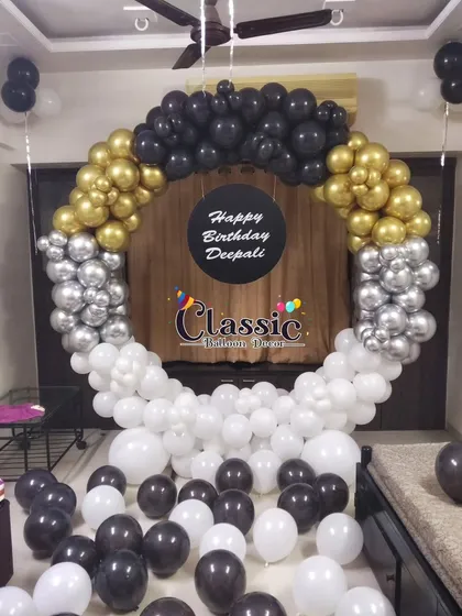 A stylish balloon ring decoration perfect for any birthday. This design features a gradient of black, gold, silver, and white balloons, with a custom 'Happy Birthday Deepali' sign in the center for a personal touch.