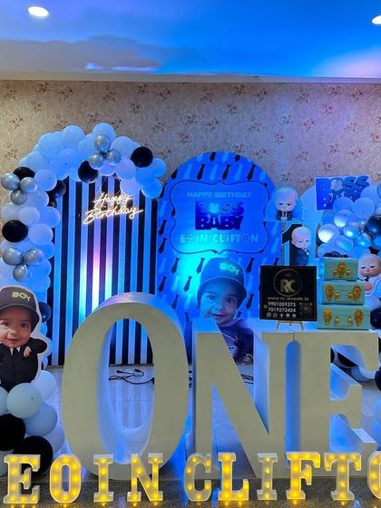 A Boss Baby themed first birthday with personalized elements. The setup includes a photo collage board and light-up marquee letters with the birthday boy's name.