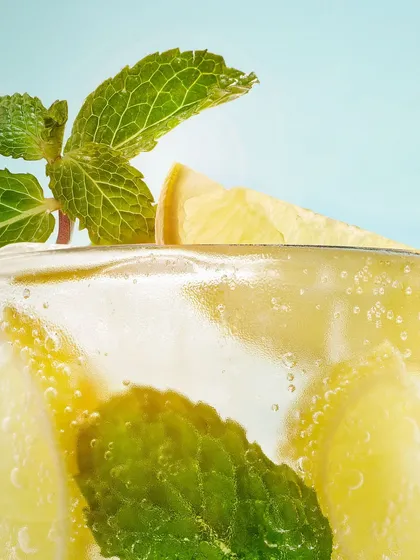 A fresh and vibrant shot of a mojito-style cocktail. The focus is on the bright green mint leaves and the condensation on the glass, making it look incredibly refreshing.
