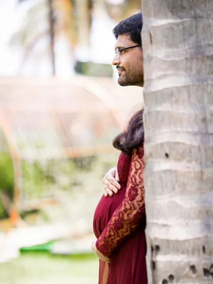 A creative and intimate shot of the couple, partially hidden behind a tree. This composition adds a sense of privacy and romance to the maternity gallery.